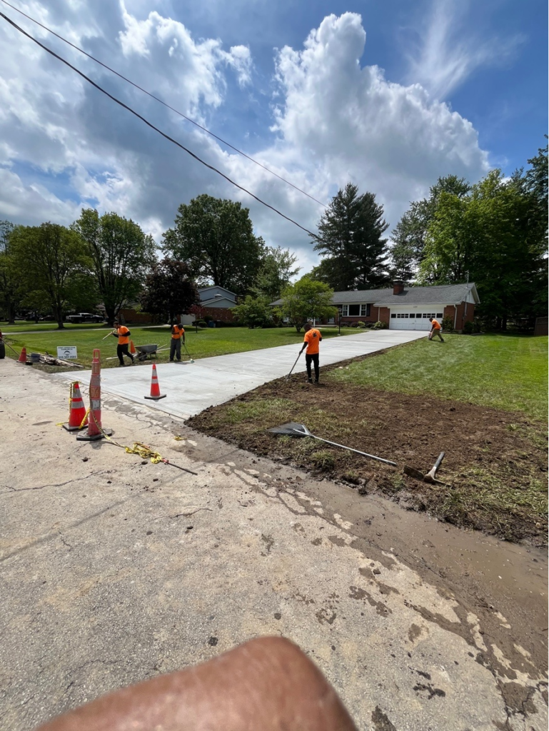 Concrete workers completing a driveway project with a home and garage in the background