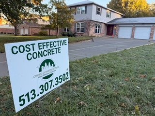 Residential driveway with a Cost Effective Concrete project sign displaying the company name and contact details